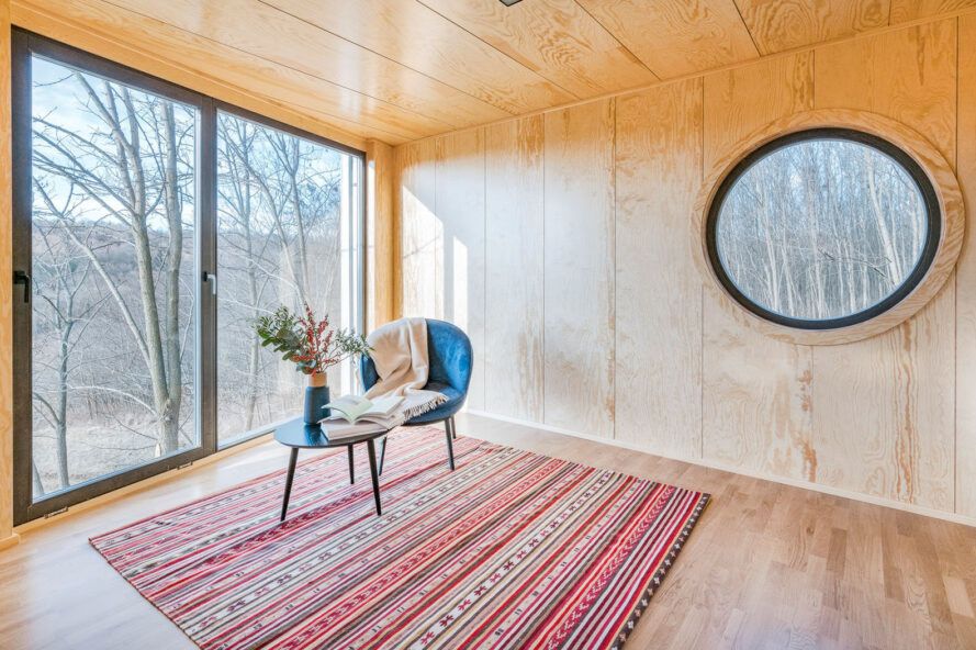Une chambre avec des murs et des sols en bois clair.  Une grande fenêtre circulaire se trouve sur le mur à côté d'une porte coulissante en verre.