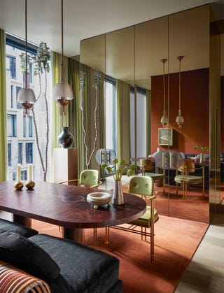 salle à manger avec deux pendentifs descendant sur une table en bois sombre entourée de deux chaises vert clair et d'une banquette bleu foncé, il y a un tapis de couleur épice et un mur est en miroir